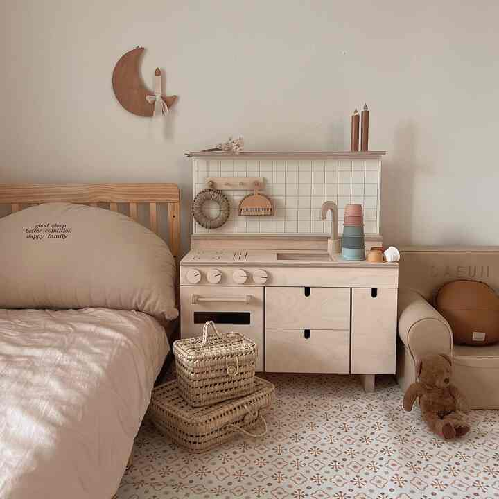 Beige and natural-toned kids' room featuring a wooden play kitchen, crib, and rattan baskets creating a cozy atmosphere