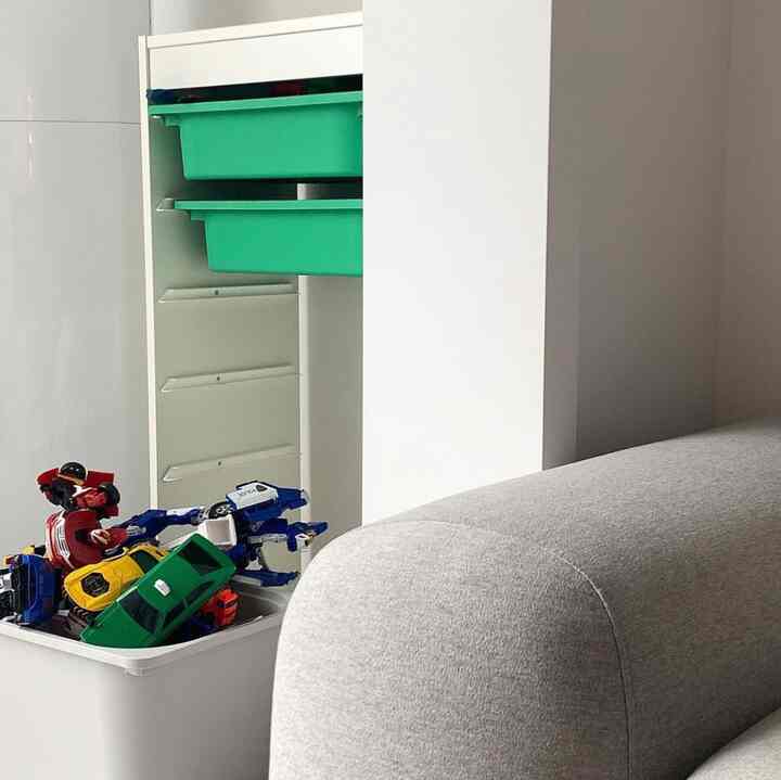 グレーのソファと子供が使いやすい緑のバスケットが並んだ白のトロファスト収納が配置されたシンプルなリビングスペース