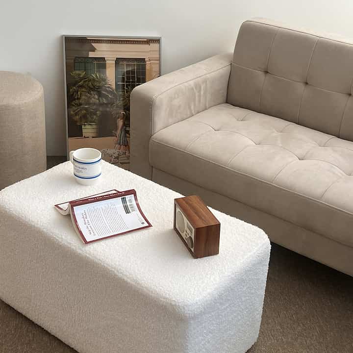 白とベージュのトーンのワンルームリビング、ブークレテーブルとミニサイズのファブリックソファが配置された雰囲気のある空間