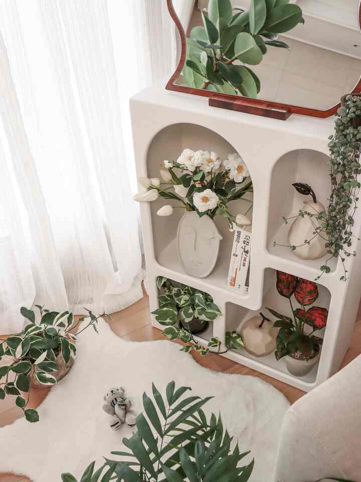 White and wood-toned living room featuring Nordic shelves and various plants creating a cozy atmosphere