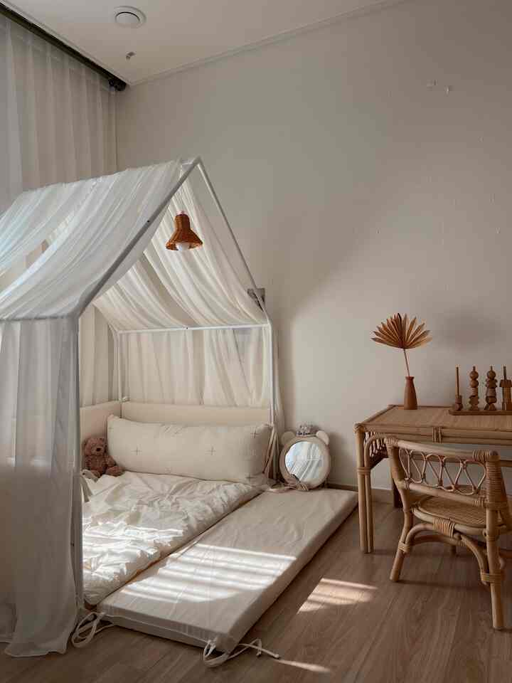 ベージュとホワイトの色調の子供部屋、低いクッションベッドとラタン家具が配置された温かみのある自然なインテリア