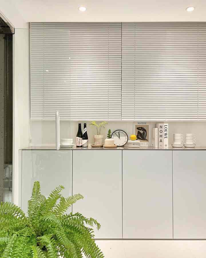 ホワイトとウッドトーンが調和したキッチン、すっきりとしたブラインドと装飾品が配置された雰囲気のあるインテリア