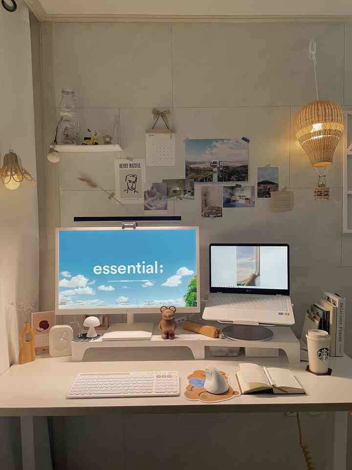 A white and natural-toned home office space featuring a clean desk with a monitor and laptop, complemented by a rattan pendant light creating a cozy work atmosphere