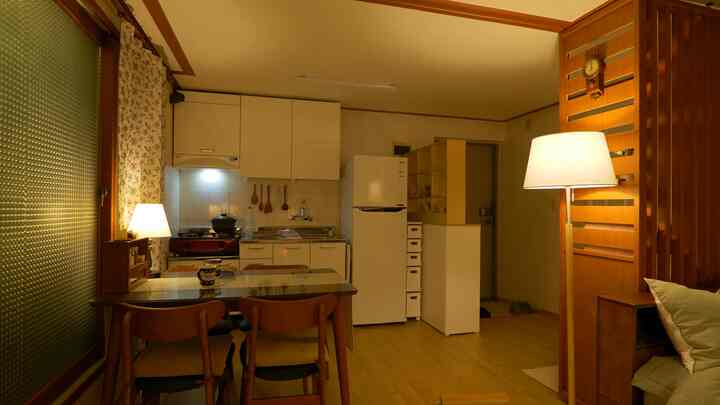 温かみのあるウッドトーンとヴィンテージカーテンが配置されたキッチンとベランダ、4人掛けのダイニングテーブルがある印象的な空間