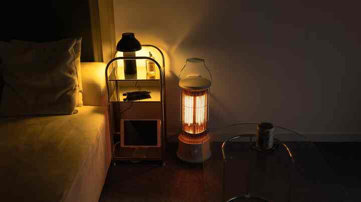 暖かい照明と白いソファ、電気ヒーターが配置された、一人暮らし向けのコンパクトなリビングルーム