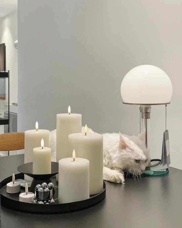 Modern kitchen space in white and black tones, featuring LED candles and a table lamp on the tabletop with a cat resting comfortably
