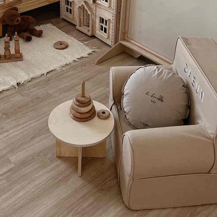 ナチュラルな木目調の床にベージュのベビー用ソファ、木製のおもちゃとラグが配置された雰囲気のある子供部屋