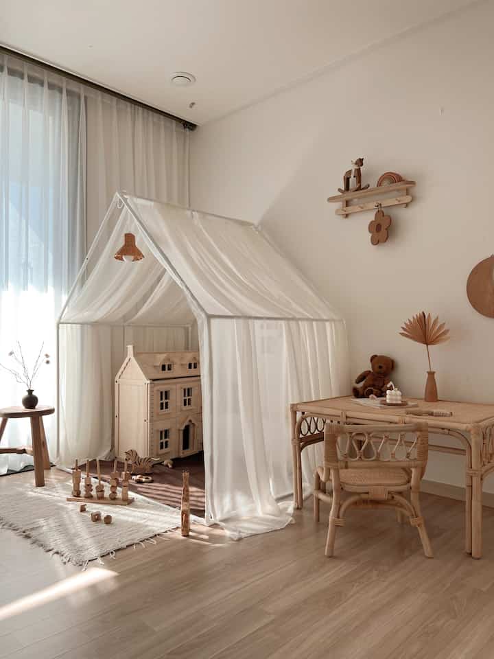 ナチュラルな雰囲気の子供部屋、白いキャノピーと木製おもちゃ、ラタン家具が配置された温かみのあるインテリア