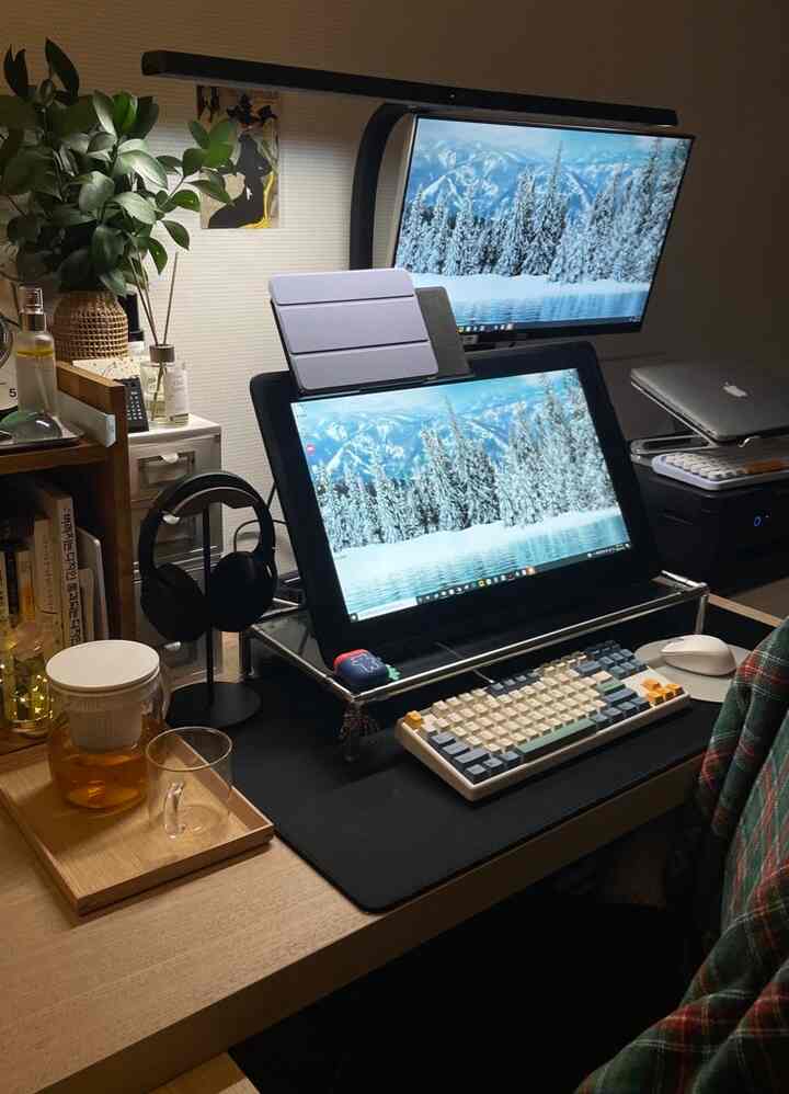 Natural wood-tone home office desk space featuring monitors, keyboard, and glass pot for warm workspace atmosphere