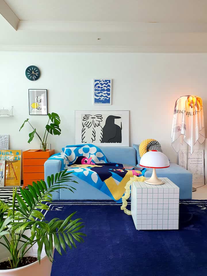 Modern living room with light sky blue sofa and blue rug, featuring posters and floor lamp creating a cozy atmosphere