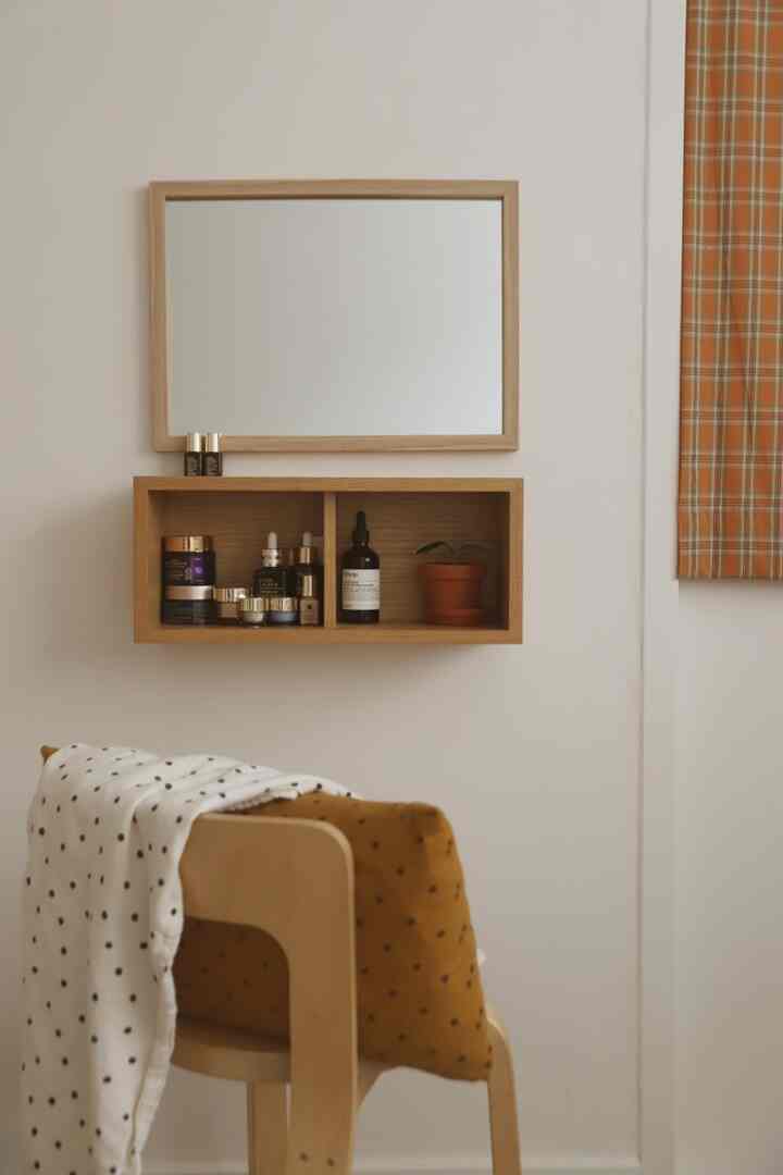 Beige and orange toned bedroom vanity space featuring a wooden shelf with cosmetics, framed mirror, and checkered curtain creating a cozy atmosphere
