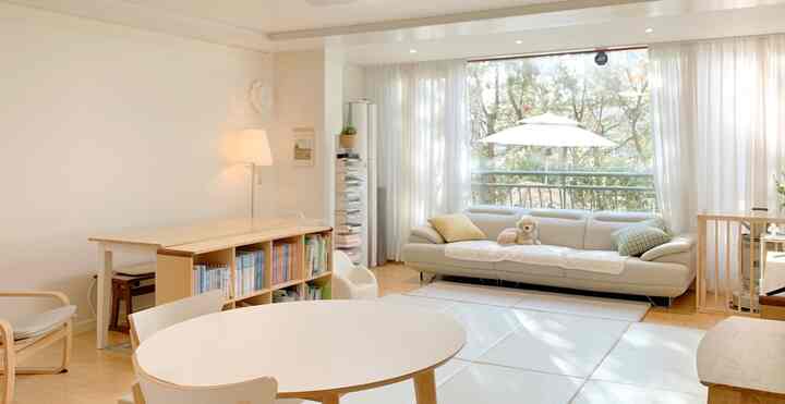 Bright white and wood-tone living room featuring large windows, bookshelves, and a cozy sofa with a warm atmosphere