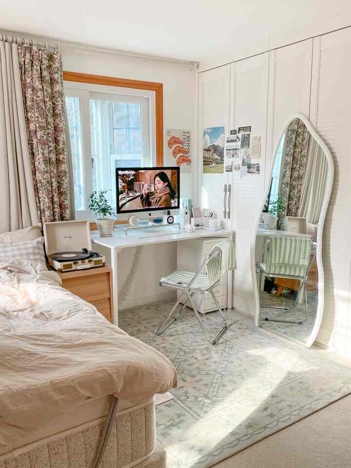 White and beige toned bedroom with home office, featuring a desk, full-length mirror, and patterned rug in a cozy atmosphere