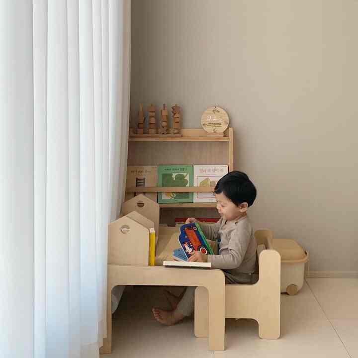 Beige wall and natural wood tone furniture in a kids' room, a toddler reading a book at the desk creating a warm atmosphere