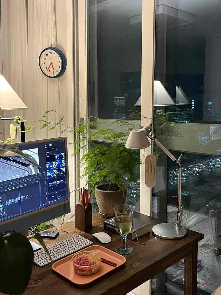 A natural-toned home office featuring wood furniture, greenery, and a cozy desk setup with computer and lamp