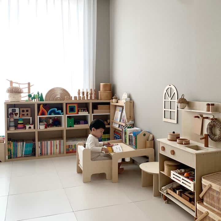 Natural tones and white tiled floor in a cozy kids' room featuring wooden furniture, bookshelves, and a child seated at a desk