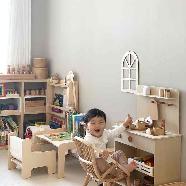 ナチュラルな木目調と明るいベージュの壁の子供部屋、子供用机とキッチン玩具が配置された赤ちゃんと暮らす温かく明るいインテリア