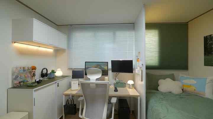 A compact bedroom and home office featuring white and green tones, organized storage cabinets, and a remote work desk with chair at center.