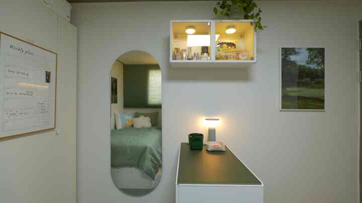 Natural-toned bedroom with white walls featuring arched mirror, vanity, closet, and a weekly planner for an organized look
