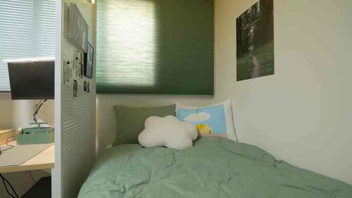 Warm green toned bedroom featuring a bed partitioned from a home office desk, creating a cozy restful space