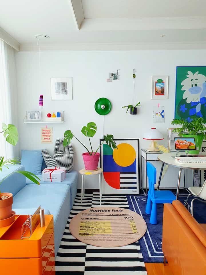 Bright living room with light blue and orange accents featuring sofa, plants, and framed art in modern mid-century modern style