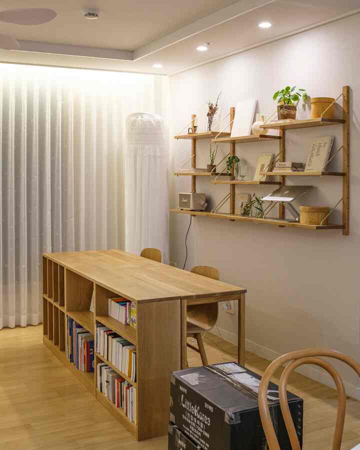 ナチュラルな色調のリビング書斎、木製のデスクと本棚が配置され、レースカーテンとフロアランプが調和した落ち着いた雰囲気のインテリア