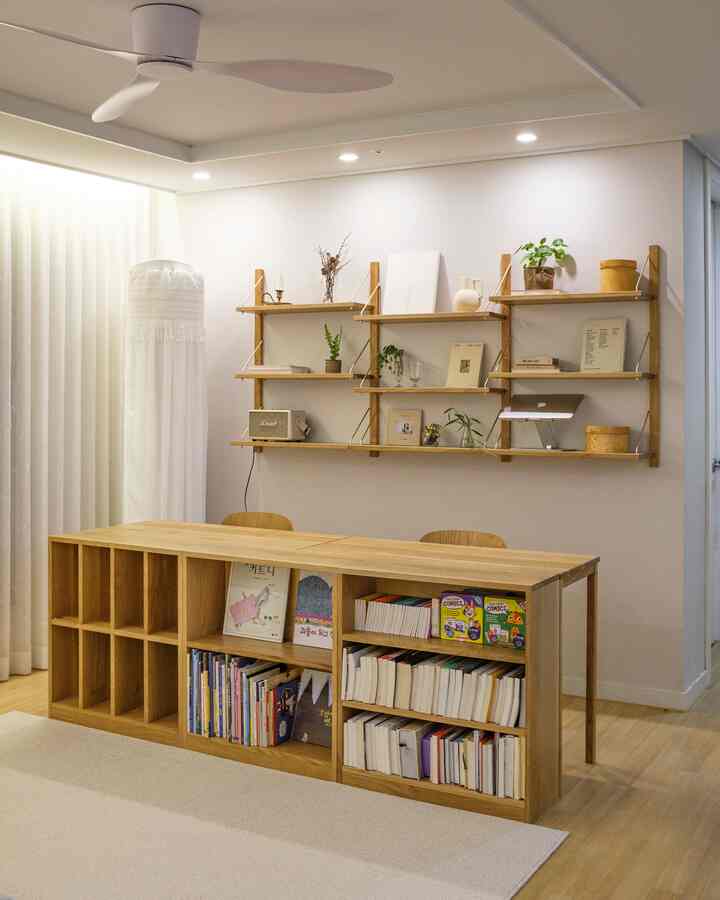 White walls and curtains, wooden bookshelves and shelves, a neat living room study area with two chairs