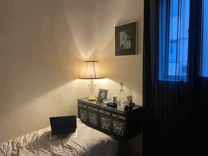 Cozy bedroom with warm table lamp light and black mother-of-pearl cabinet, white duvet cover and black curtains create a vintage atmosphere