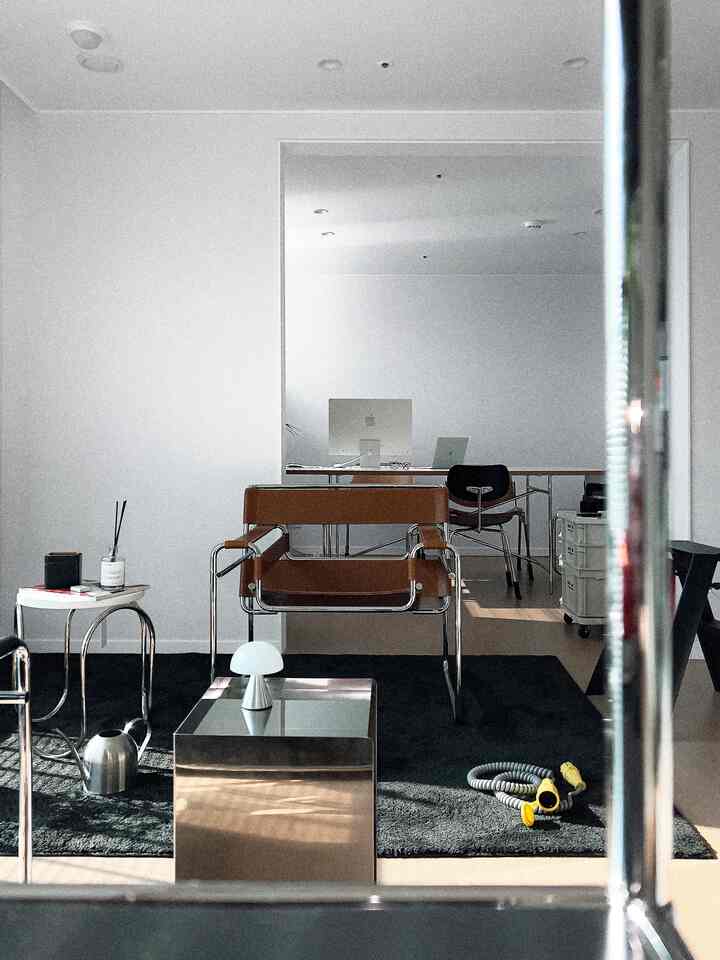 Modern living room with white walls and a black rug, featuring brown leather armchair and minimalistic lighting creating a sleek atmosphere