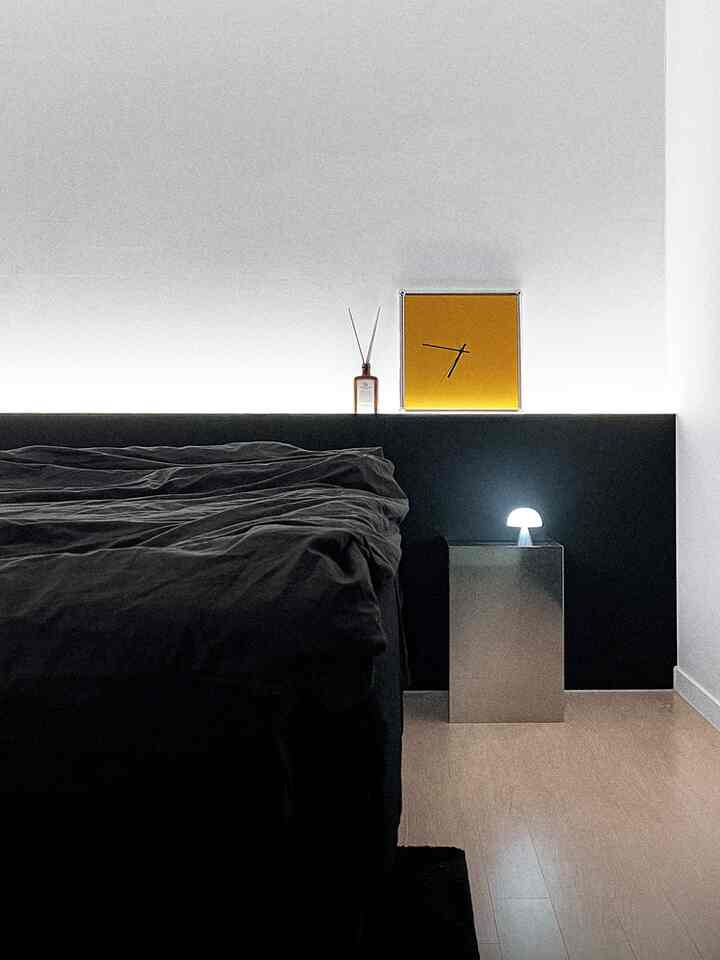 A modern and simple black and white bedroom featuring a low black headboard and minimal nightstand lamp arrangement