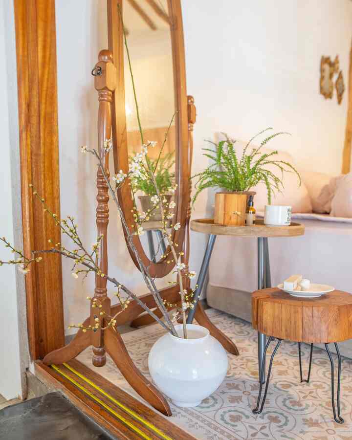 Cozy bedroom with warm wood tones and white walls, featuring a standing mirror, potted plants, and a patterned rug creating a vintage atmosphere