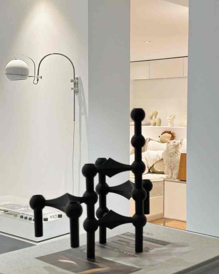 White and beige toned bedroom featuring a wall sconce on left wall and a cat perched on furniture right-center, creating a cozy atmosphere