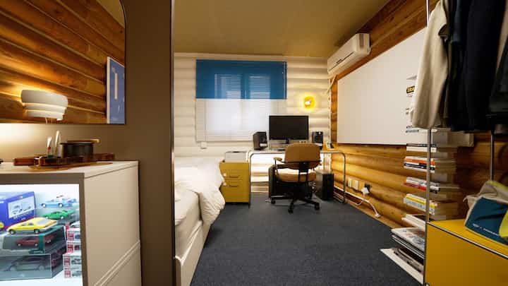 Natural brown-toned log cabin bedroom and home office with desk, office chair, blinds, and storage creating a cozy room