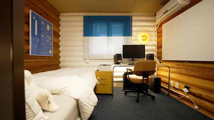 白と青のトーンでまとめられたワンルームの寝室兼在宅勤務スペース、ミッドセンチュリーモダン家具、ブラケットライト、足元ヒーターが配置された雰囲気のあるインテリア