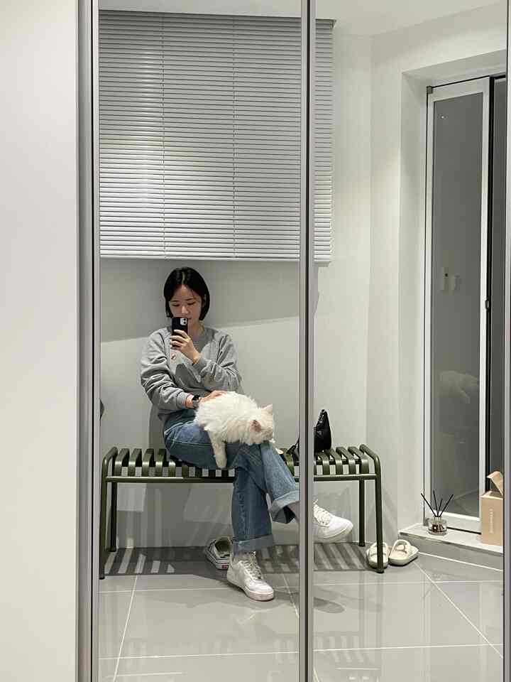 A white and gray toned entrance featuring a green bench where a woman sits holding a white cat on her lap in a tidy space