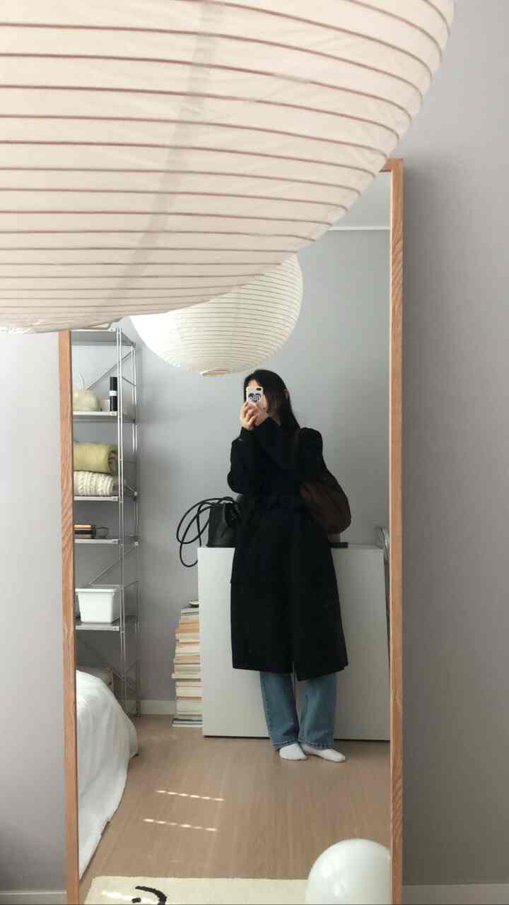 A minimal bedroom with light gray walls, wooden full-length mirror, metal shelving, and neat storage cabinet