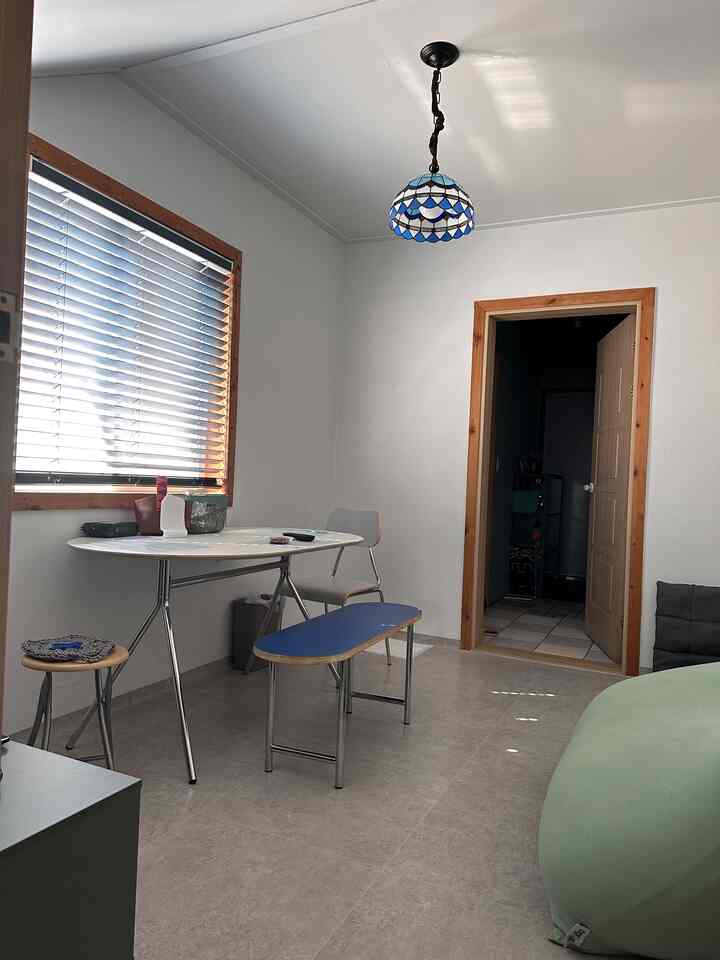 白い壁と木目調のドア枠、ミッドセンチュリーモダンのダイニングテーブルと椅子が配置されたコンパクトな休憩室