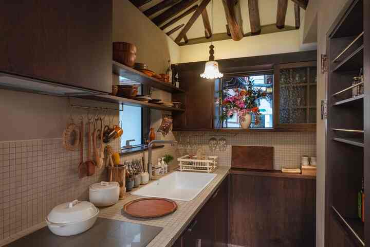 ダークウッド調とホワイトタイルのヴィンテージ風キッチン、木製の天井梁と中央のペンダントライトが配置された空間