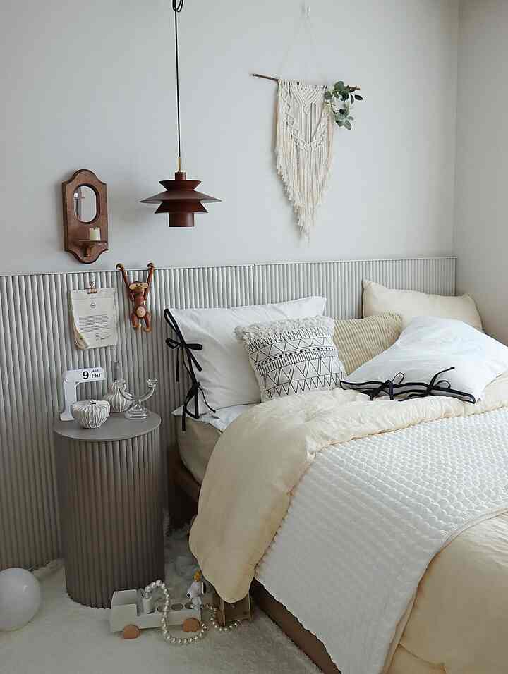 White and beige toned bedroom featuring mid-height stool, pendant light, and macrame decoration creating a cozy natural space