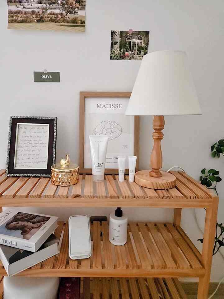 Natural wood tone shelf with table lamp and picture frames in a simple and clean space