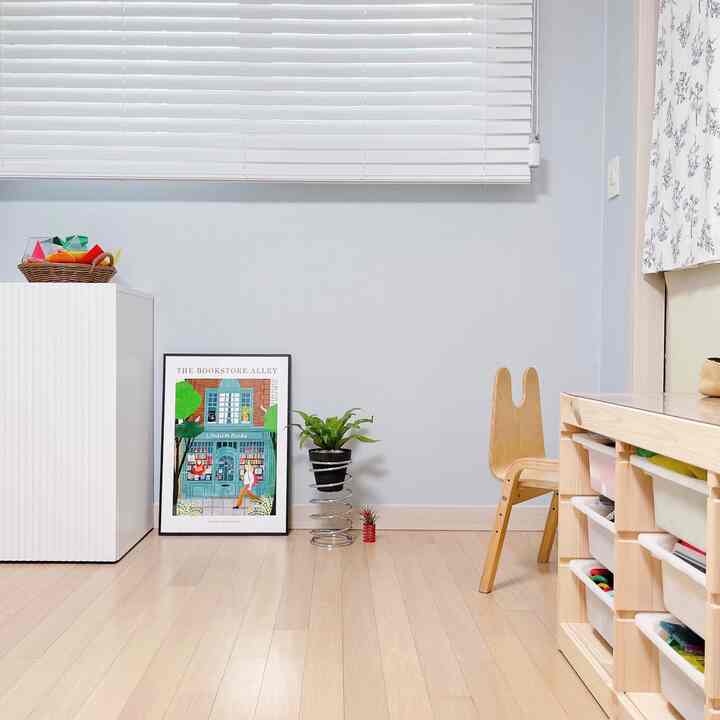 Kids' room with white walls and blinds, wood-tone flooring and furniture, featuring organized storage bins and a child-sized wooden chair, creating a natural atmosphere