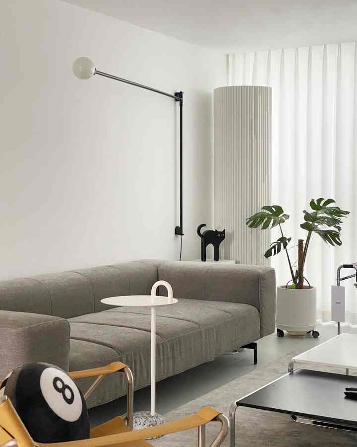 Natural-toned living room featuring a gray sofa, white side table, and monstera plant with a simple and modern design