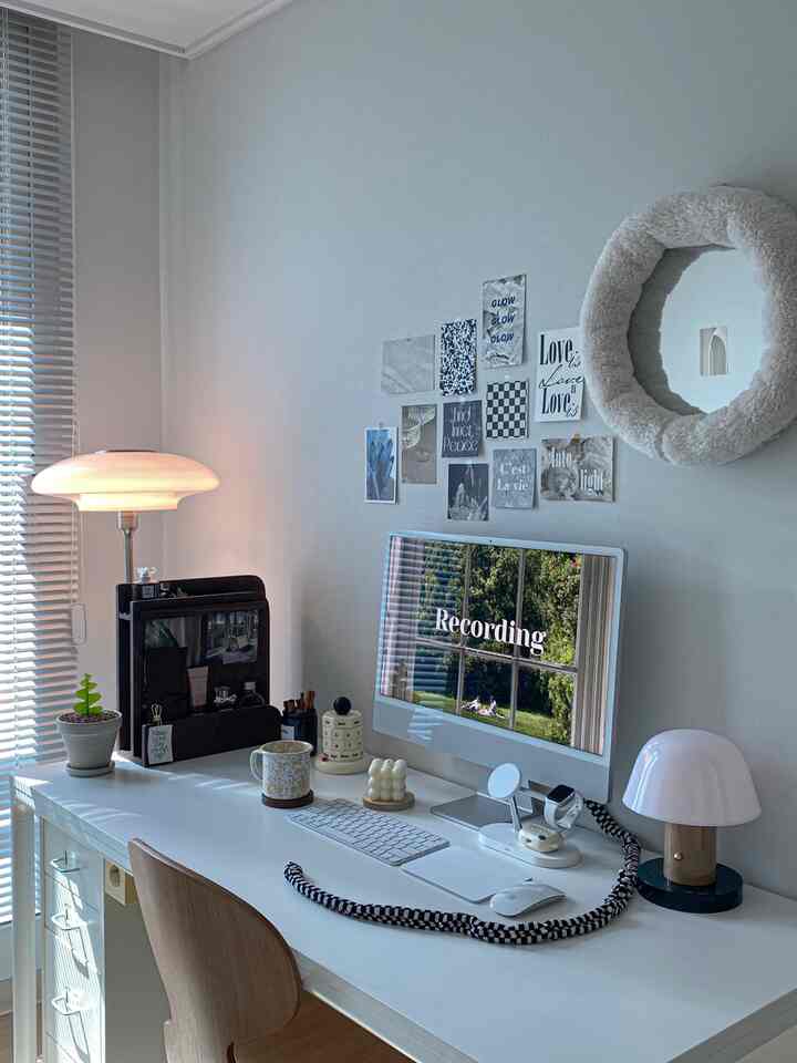 Modern and simple home office in white and wood tones, featuring a clean desk setup, table lamps, a round mirror, and artistic frames on the wall