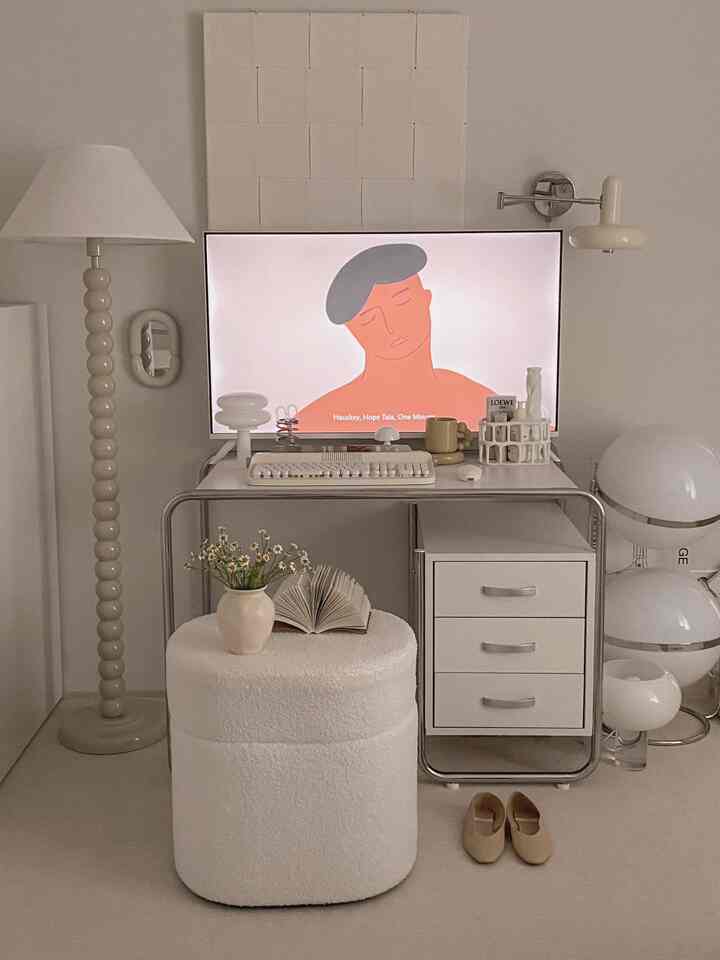 Natural modern white-toned studio apartment home office space featuring a simple white desk, stool, and various lighting fixtures creating a cozy atmosphere