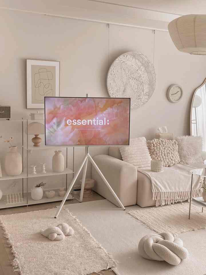 Soft white tone living room featuring a white sofa and tripod TV stand, presenting a cozy and clean space