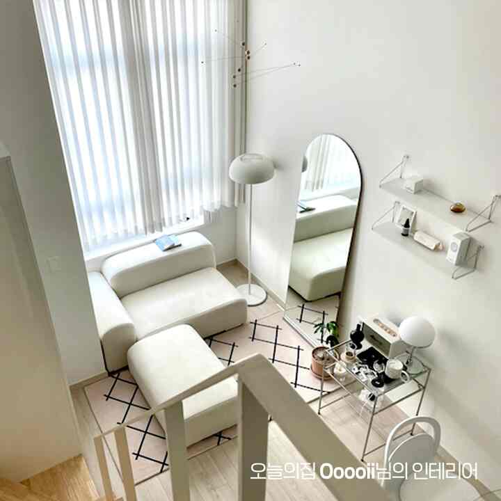 白とベージュ調のすっきりとした小さなリビング、ソファと鏡が配置されたモダンで清潔感のあるインテリア