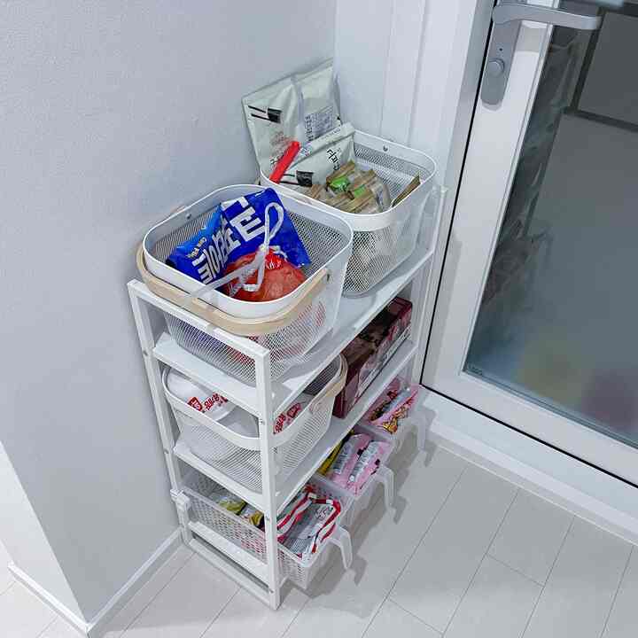 White-toned compact kitchen space featuring IKEA storage shelf and multipurpose metal baskets neatly organizing food ingredients