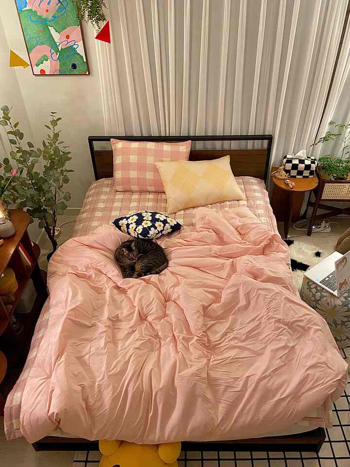 A cozy pink and white toned bedroom featuring a bed with a cat and soft bedding, accented with natural wooden elements.