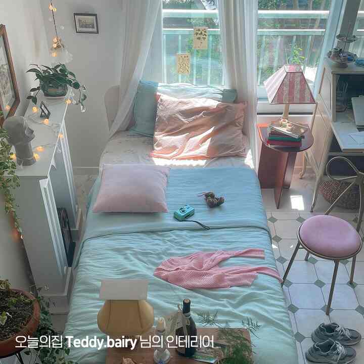 ピンクとベージュの色合いが調和する小さな寝室、ベッドとナイトテーブル、デスクが配置された温かみのある空間