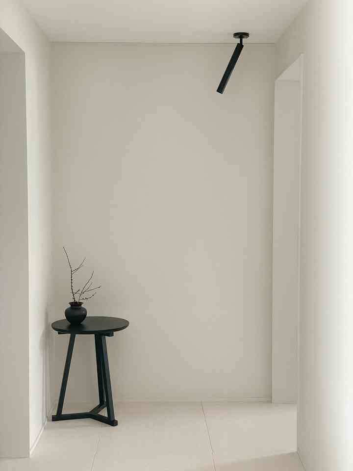 A clean white-toned hallway featuring a black side table with a vase on the left, showcasing a simple minimalist interior